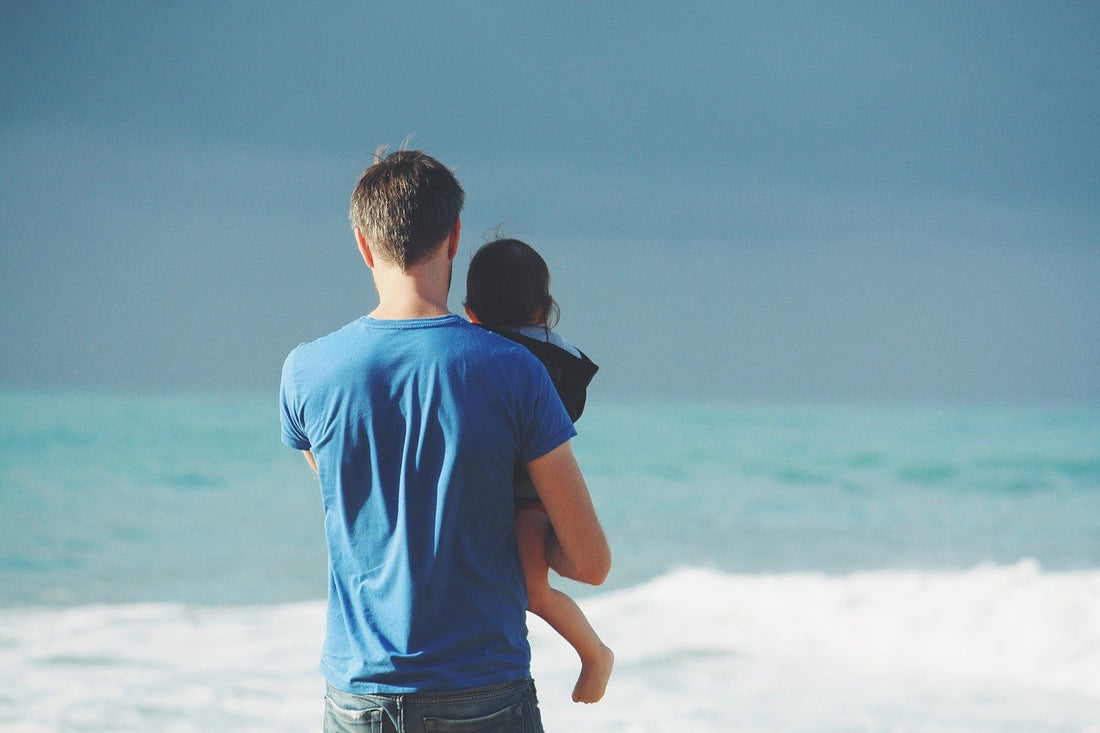 dad holding child beach ocean watching