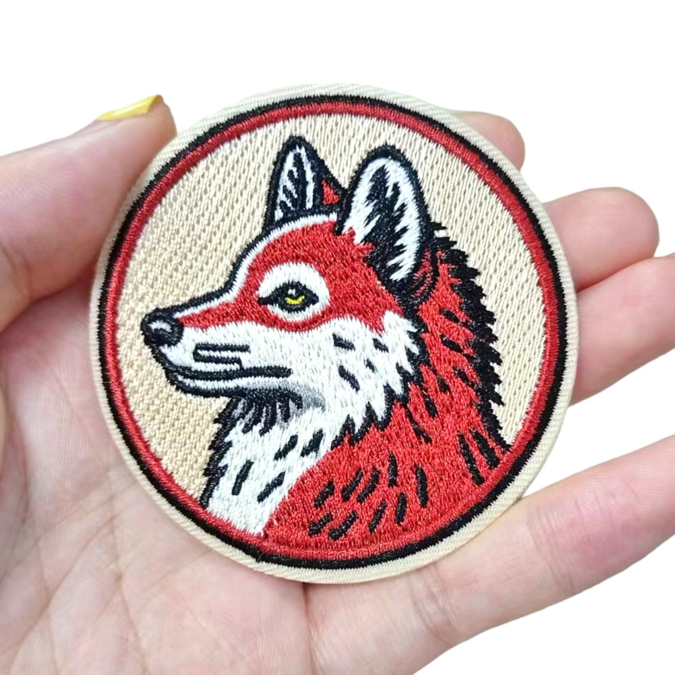 Embroidered patch of a fox head held in a hand on a white background