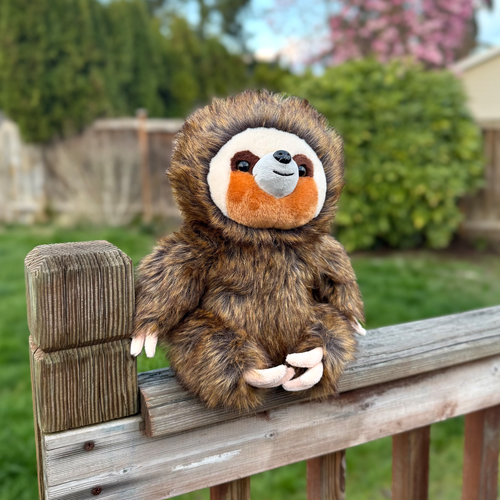 Sloth stuffed animal on fence with a garden as the background
