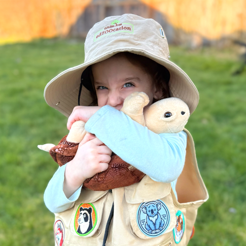 A little girl with a field hat and vest hugging a Tortoise stuffed animal